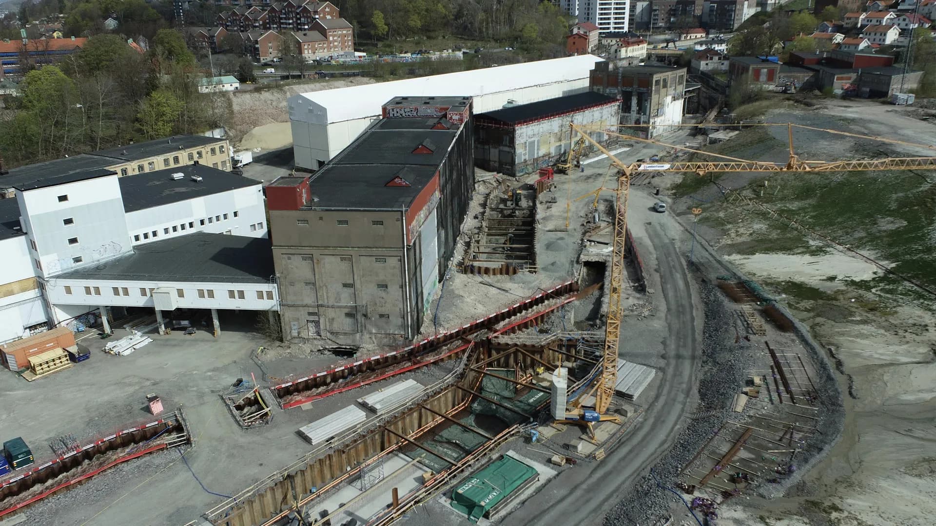 Drönarfoto över bygget i Forsåker i Mölndal: de gamla pappersbruksbyggnaderna, spontade schakter för forsens nya fåra och en byggkran