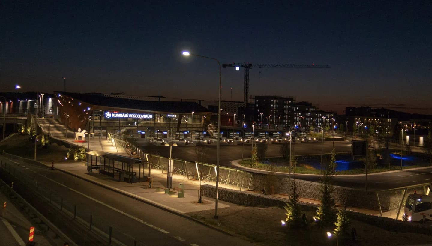 Kungälvs resecentrum i kvällsbelysning med busshållplatser, planteringar och ny bebyggelse i Kongahällaområdet
